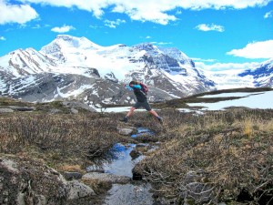 Person jumping over a river with a mountain in the background